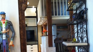 A narrow hallway with a wooden floor, a kitchen area with a black refrigerator, and a decorative figure on the left. - Unusual, Charming 16th Century Apt Near Place Des Vosges (Paris)