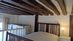 A bedroom with a wooden bed frame, a nightstand with a lamp, and a window with curtains. - Unusual, Charming 16th Century Apt Near Place Des Vosges (Paris)