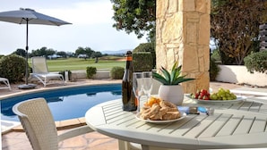 Ein Tisch am Pool mit einer Flasche, Gläsern, Brot, Obst und einer Topfpflanze.