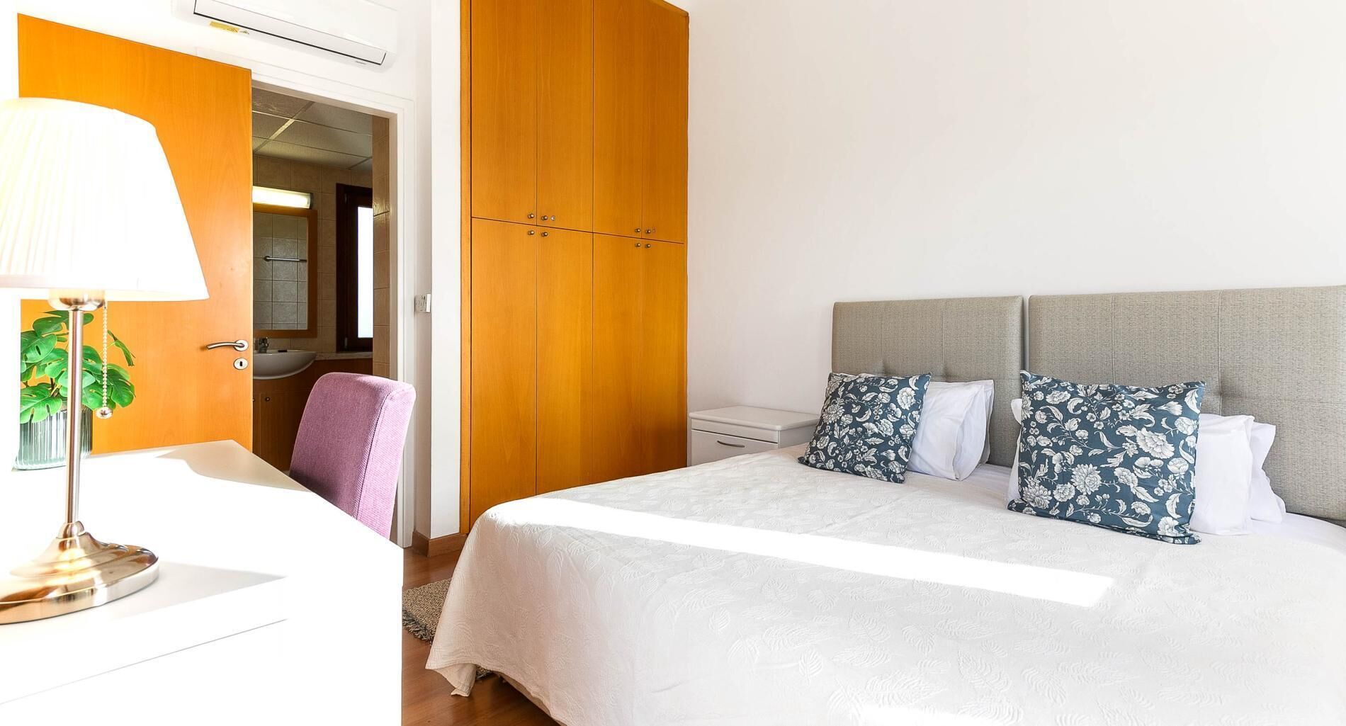 A hotel room with a bed, a desk, a chair, a wardrobe, and a bathroom visible through an open door.