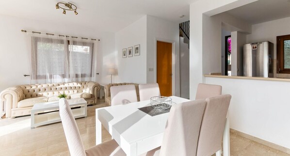 Una sala de estar moderna con un sofá color beige, una mesa de centro blanca y un comedor con una mesa blanca y sillas color beige.
