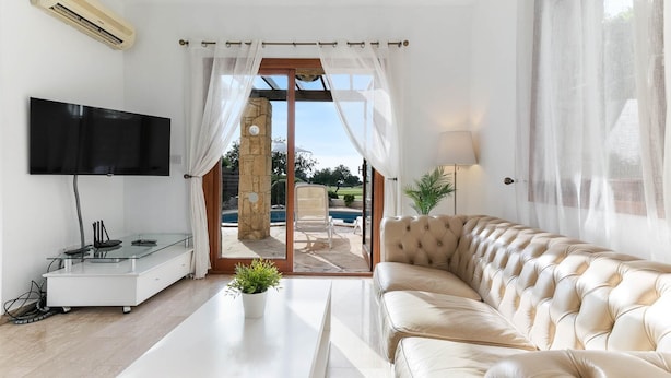 Ein modernes Wohnzimmer mit einem Flachbildfernseher, einem Glastisch, einer Ledersofa und Blick auf ein Außenbecken durch eine Glasdoor.
