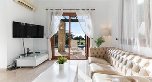 Una sala de estar moderna con un televisor de pantalla plana, una mesa de centro de vidrio, un sofá de cuero y vistas a una piscina exterior a través de una puerta de cristal.