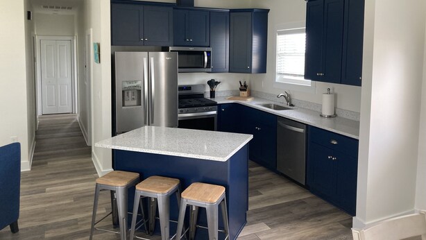Una cocina moderna con armarios azul oscuro, un refrigerador de acero inoxidable, un microondas y un horno empotrado. Hay tres taburetes en la isla y una ventana que proporciona luz natural.
