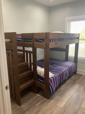 A bunk bed with a wooden ladder, a striped bedspread, and a window with blinds.