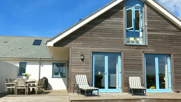 Een tweelaags huis met een terras, een eethoek met tuinmeubilair en twee comfortstoelen.
