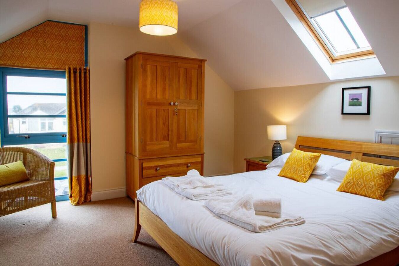 Een slaapkamer met een groot bed, een houten garderobe, een rieten stoel en een dakvenster.