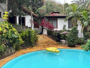 A pool with a yellow inflatable ring, surrounded by lush greenery and a staircase leading to a building. - House Season Refugio Teresopolis, surrounded by forest, environmental protection area (Quebra Frascos)