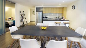 A modern kitchen with stainless steel appliances, a dining area with a dark table and white chairs, and a small living area with a bed and a ladder. - 250m from the beach.Gym/lap pool access,Parking, pet friendly, outdoor area, BBQ (Port Melbourne)