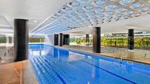 A modern indoor swimming pool with clear blue water, surrounded by black columns and a patterned ceiling. - 250m from the beach.Gym/lap pool access,Parking, pet friendly, outdoor area, BBQ (Port Melbourne)