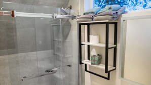 A modern bathroom with a glass-enclosed shower, a toilet, a sink, and a shelf with towels.