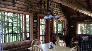 L’intérieur d’une cabane en rondins, avec une table à manger, des chaises, un canapé et de grandes fenêtres donnant sur la forêt.