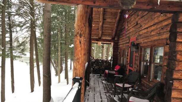 Une cabane en bois avec un porche, un sol recouvert de neige et une vue sur une forêt.