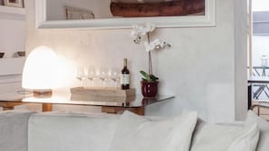 Una sala de estar moderna con un sofá blanco, una mesa de centro de vidrio, un espejo y una orquídea en maceta.