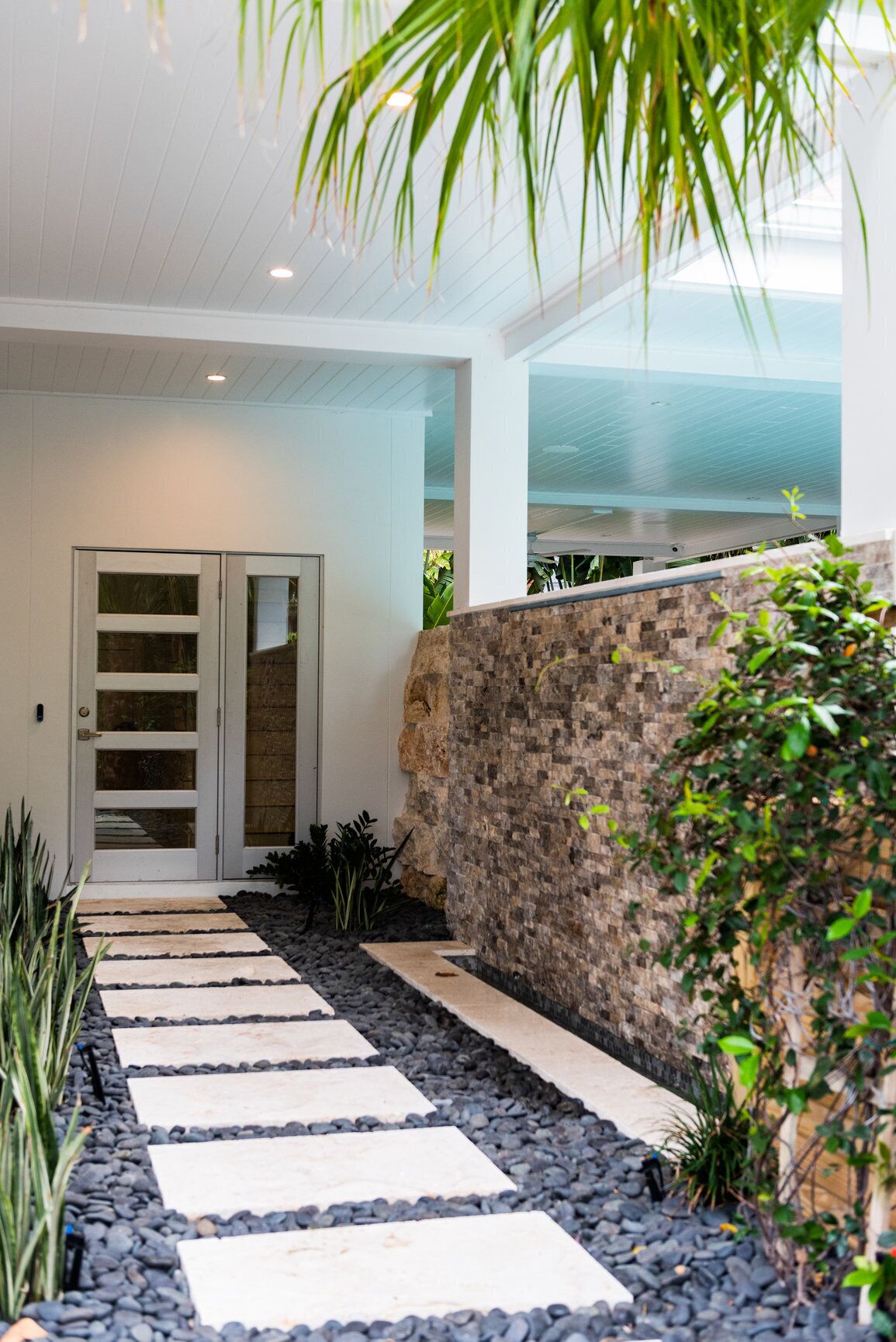 A modern entryway with a stone wall, a glass door, and a stone pathway leading to a door.