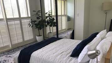 Een slaapkamer met een bed, een bedlampje, een plant in pot en een raam met zonwering.
