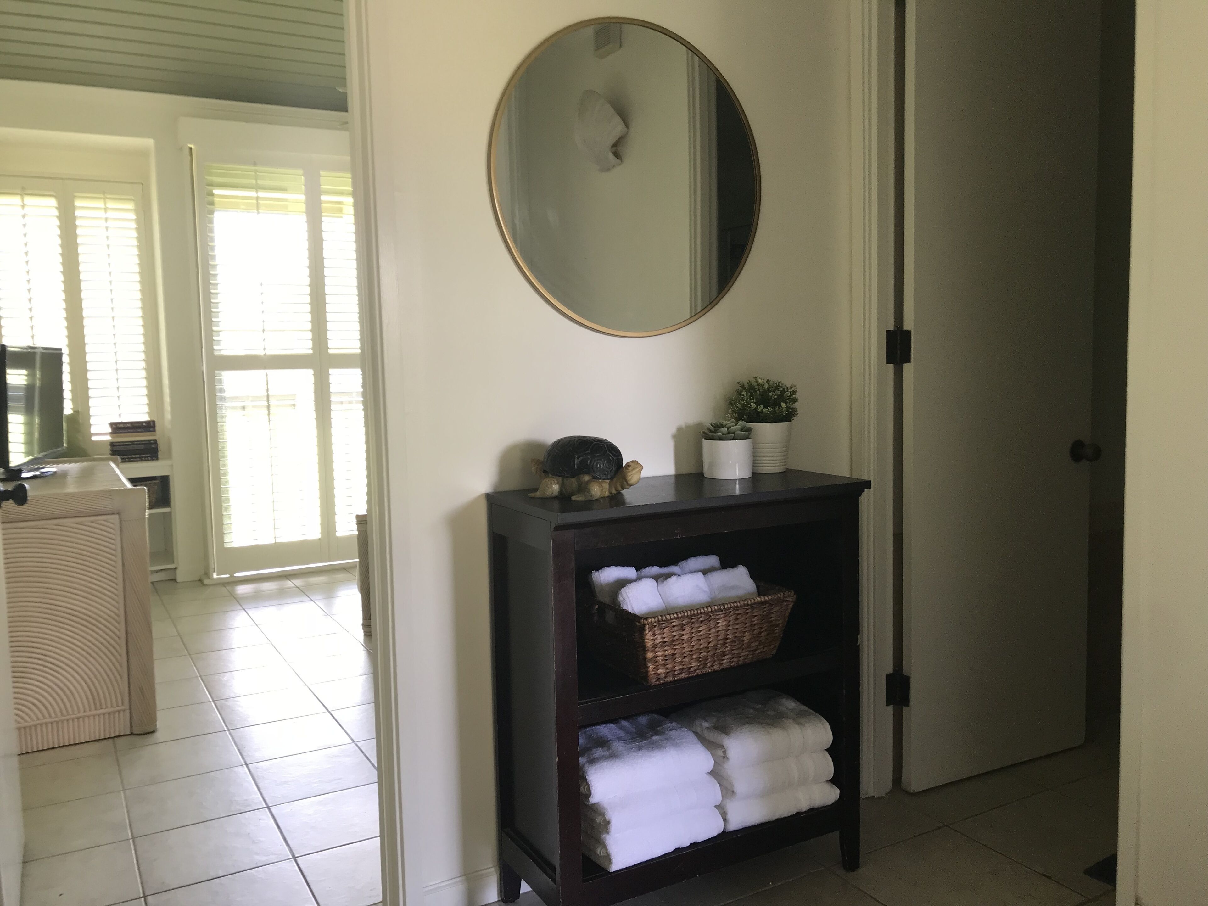 Een gang met een donkere houten console tafel, een spiegel en een mand met opgevouwen handdoeken.