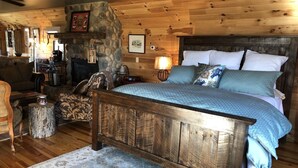 A rustic bedroom with a wooden headboard, a stone fireplace, and a cozy seating area with a lamp. - THE HAY LOFT in the Beautiful Shenandoah Valley (Mt Jackson)