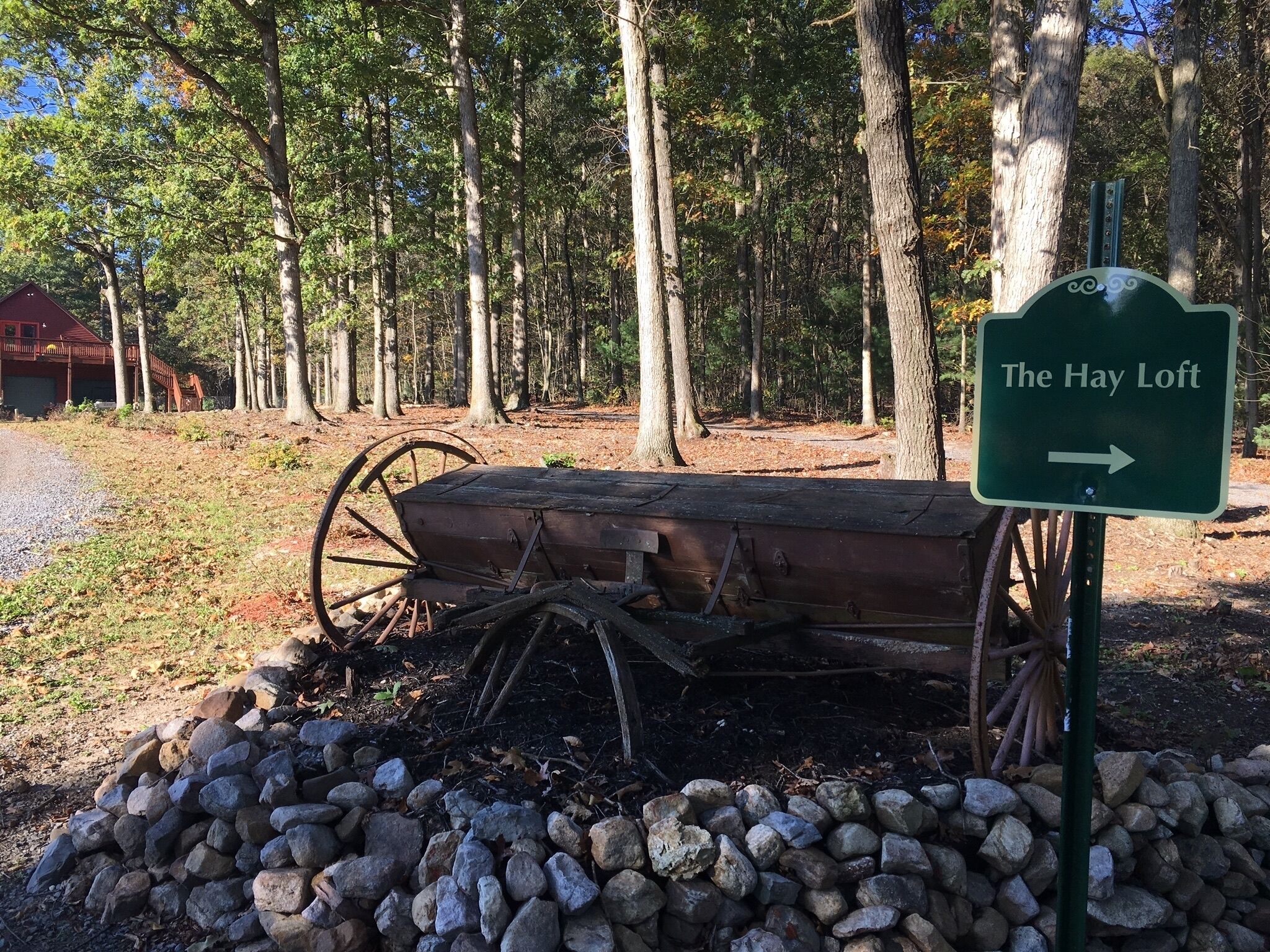 A wooden hayloft sign with an arrow pointing to the right, surrounded by a pile of rocks and a wooden cart.
