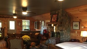 A cozy cabin interior with a wooden floor, a stone fireplace, a dining area, and a living room with a couch and chairs. - THE HAY LOFT in the Beautiful Shenandoah Valley (Mt Jackson)