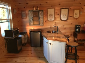 A compact kitchen with a microwave, refrigerator, sink, and bar stool.