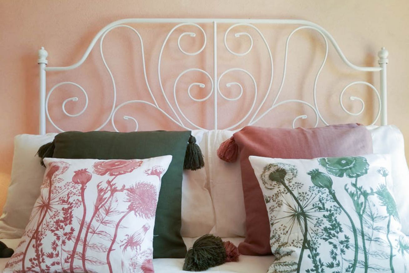 Un lit avec une tête de lit en métal blanc et trois coussins décoratifs ornés de motifs floraux.