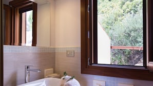 A bathroom with a large sink, a mirror, and a window with a view of greenery.