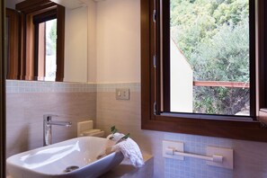 A bathroom with a large sink, a mirror, and a window with a view of greenery.