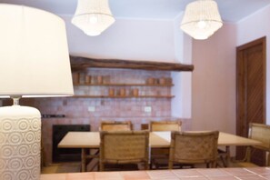 A dining area with a table and chairs, a hanging lamp, and a brick wall with shelves.
