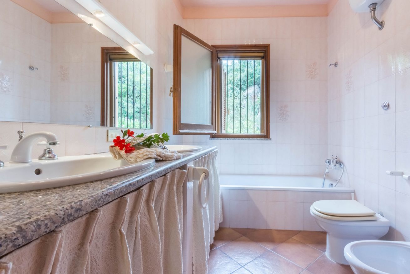 Ein Badezimmer mit Waschbecken, Spiegel, Fenster, Badewanne und Toilette.