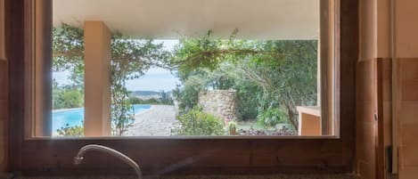 A kitchen with a sink and a view of a pool and garden through a window.