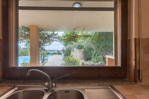 A kitchen with a sink and a view of a pool and garden through a window.