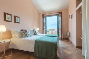 A bedroom with two beds, a nightstand, a window with a view, and a door leading to an outdoor area. - VILLA BELLAVISTA with private pool and sea view, a few km from Villasimius (Villasimius)