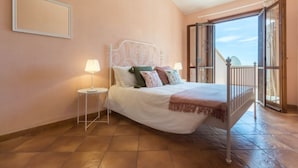 A bedroom with a bed, nightstands, a balcony with a view, and a door leading outside.