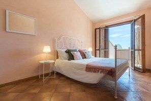 A bedroom with a bed, nightstands, a balcony with a view, and a door leading outside.