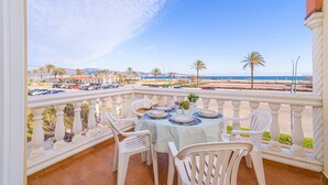 Un balcon avec une table dressée pour le dîner, donnant sur une plage bordée de palmiers et un espace de stationnement.
