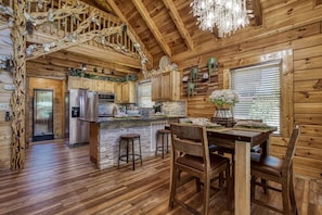 Cozy cabin features a central kitchen island, wooden staircase, and chandelier.