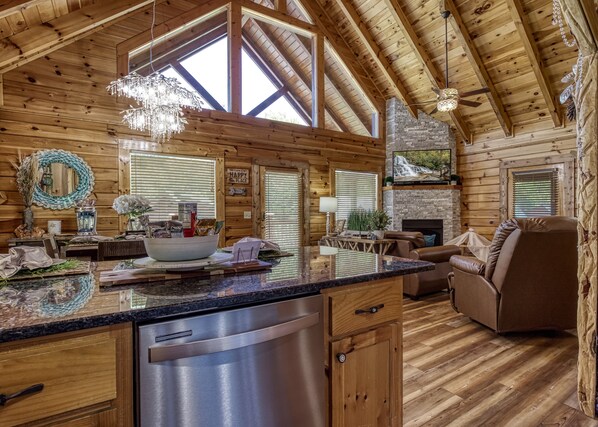 Cozy cabin-style interior with a kitchen area, comfortable seating, and a high ceiling with exposed beams.