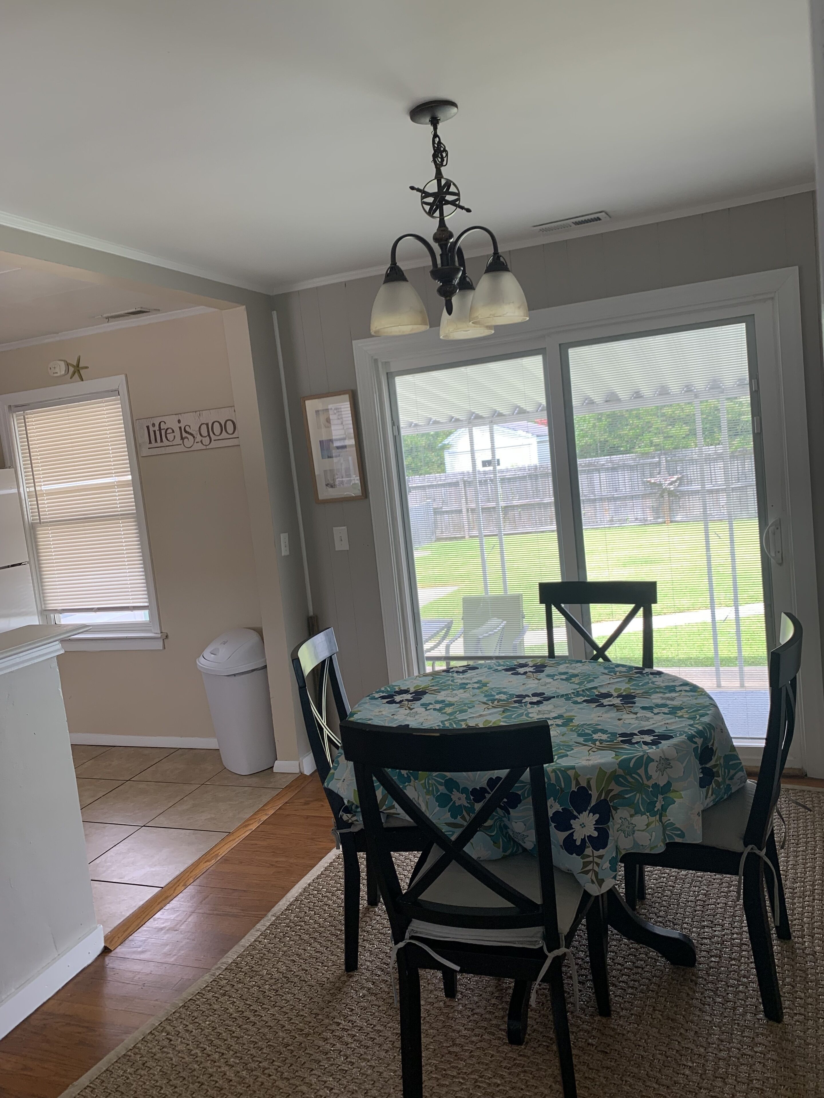 A dining area with a table and chairs, a ceiling light fixture, a trash can, a refrigerator, and a window with blinds.
