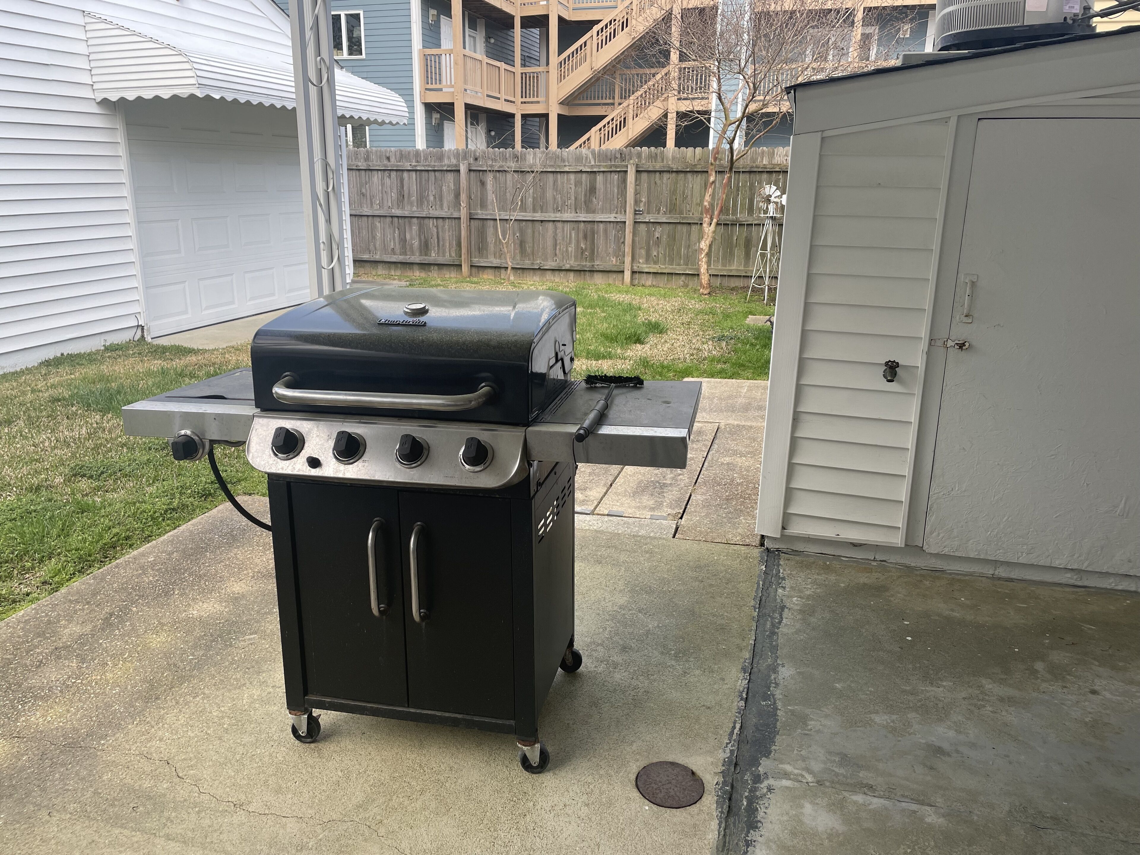 A portable grill with four burners and a side table, placed on a concrete patio.