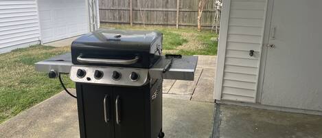 A portable grill with four burners and a side table, placed on a concrete patio.