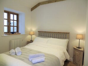 Ein ordentlich bezogenes Bett mit Kissen und Handtüchern, zwei Nachttische mit Lampen, ein Fenster mit Aussicht und ein Holz-Kopfschild.