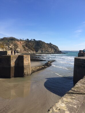 Eine Küstenlandschaft mit einer felsigen Klippe, einem Sandstrand und einer Steinmauer.
