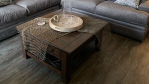 A modern living room with a sectional sofa, a coffee table with a decorative tray, and a painting of a boat on the wall. - The Club at Mexico Beach - Our Happy Place (Mexico Beach)