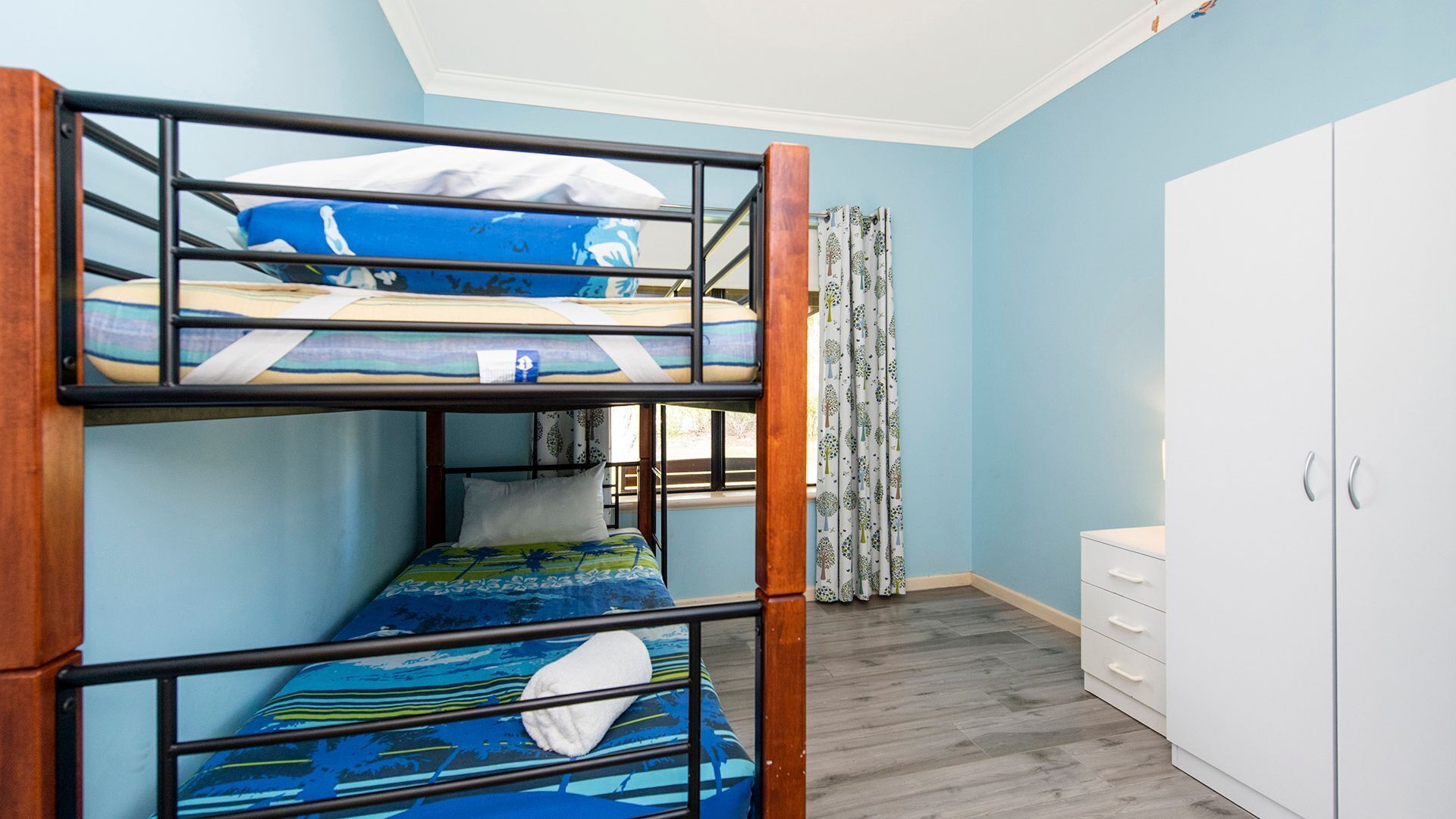 A bunk bed room with a white wardrobe and a window with curtains.
