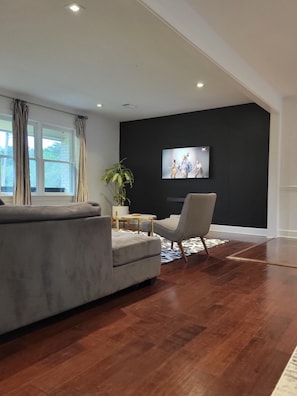 Un salon moderne avec un canapé gris, une table basse et un téléviseur fixé à un mur foncé.