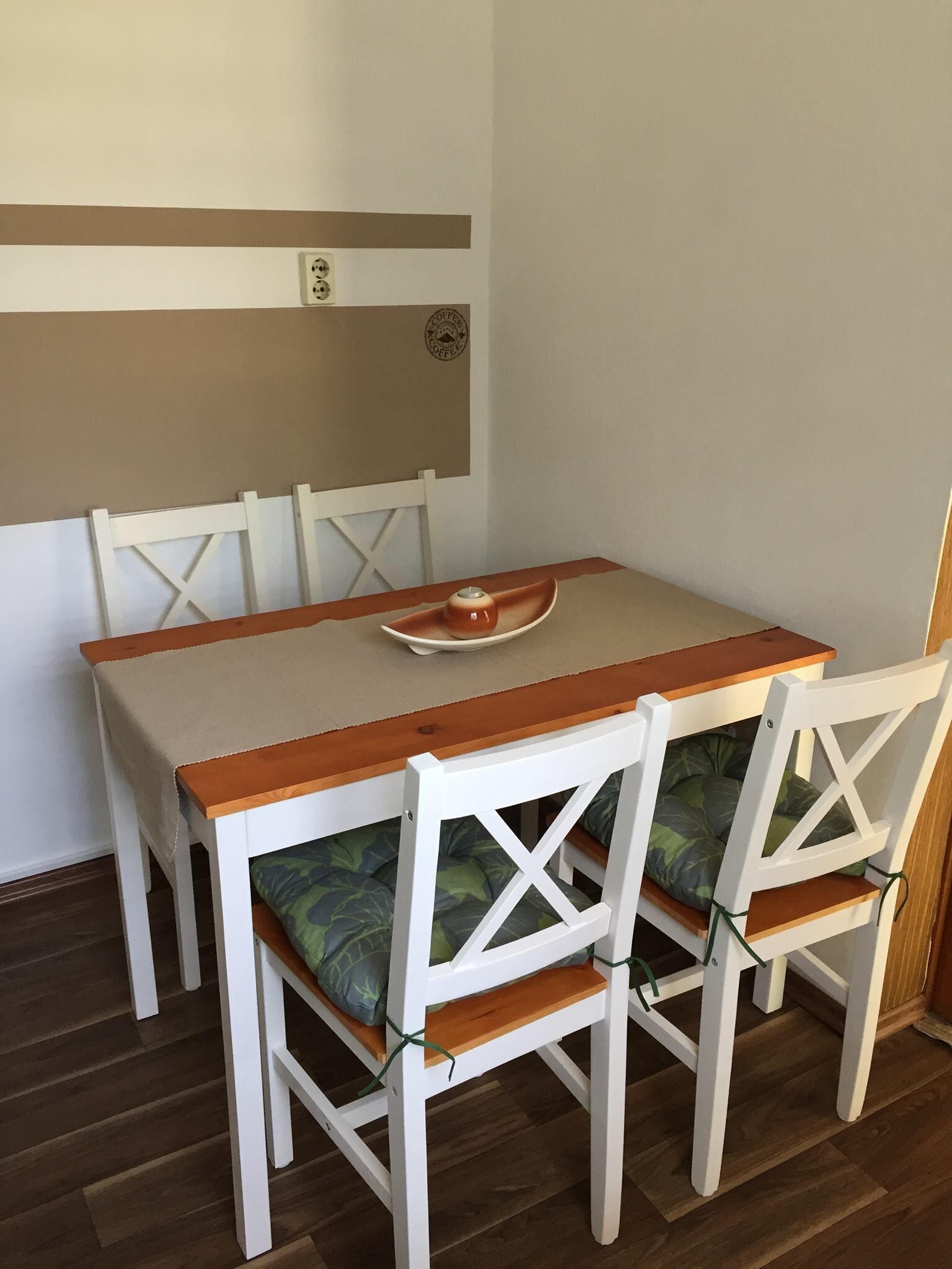 A dining table with four white chairs, each with a green cushion.