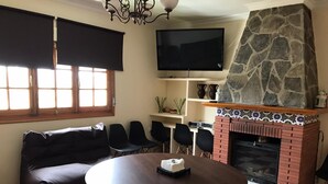 Olohuoneessa on kivinen takka, pyöreä pöytä, sohva ja seinälle asennettu televisio.