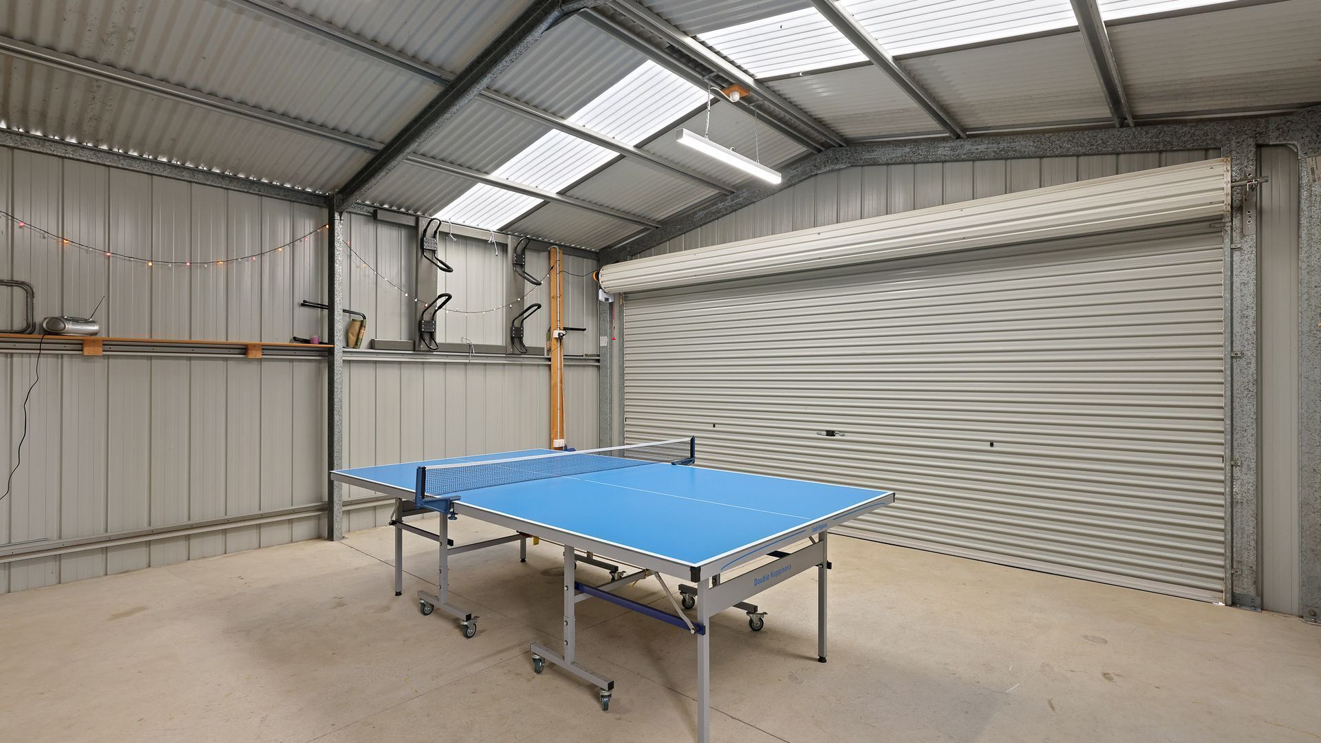 Une table de ping-pong dans une vaste pièce d’usine, avec une grande porte de garage et des murs en métal.