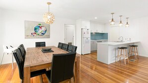 Una cocina moderna con armarios blancos, una mesa de comedor de madera y sillas negras, y lámparas colgantes.